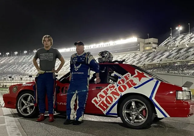Two drivers beside the red Laps of Honor Fox-body Mustang at a speedway at night