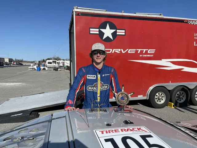 Driver in a race suit beside race car number 105, a Corvette team transporter behind him