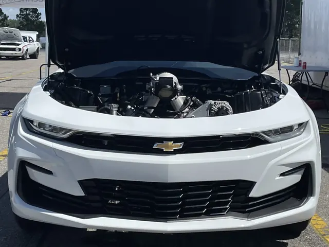 The white COPO Camaro with its hood open showing the engine