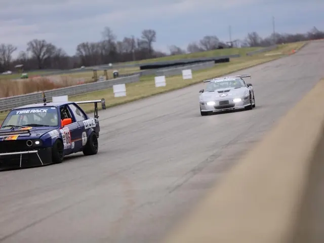 Race cars on a road course, a blue car leading a silver Corvette