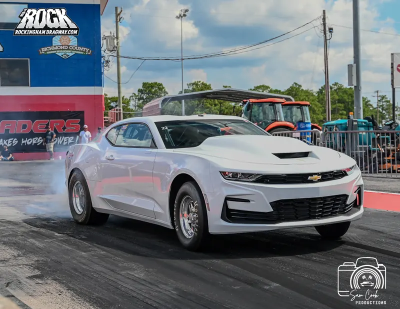 White Chevrolet COPO Camaro drag car launching off the line at Rockingham Dragway, tire smoke trailing behind the rear wheels